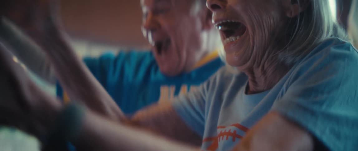 An elderly couple celebrating a win while watching sports in a living room during daytime