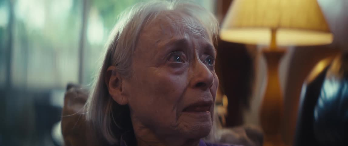 An elderly woman holding a cellphone looking upward sadly with tears in her eyes