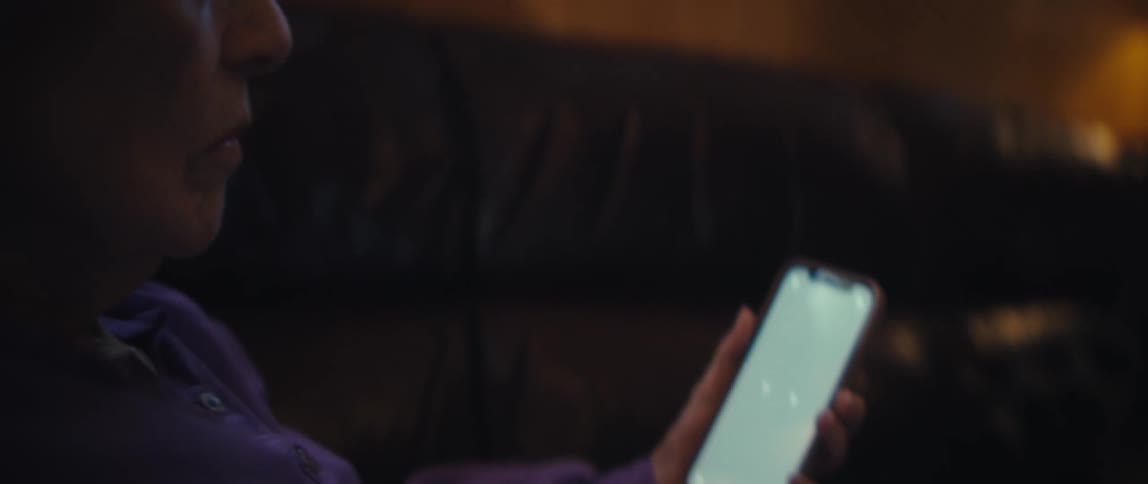 Elderly woman sitting on dark couch attentively looking at handheld device screen
