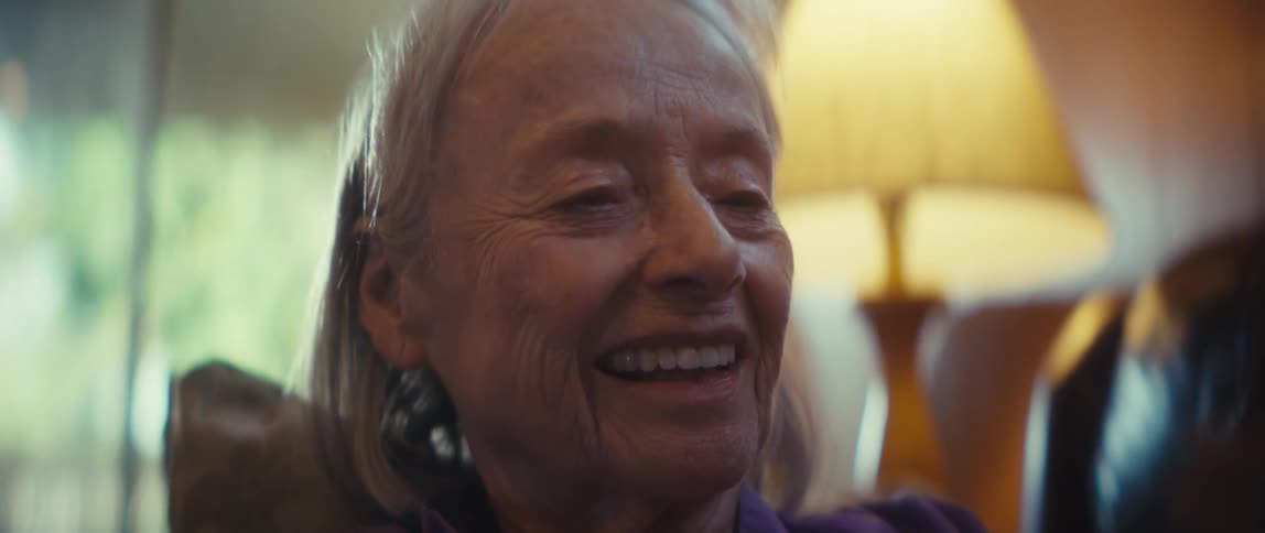 An elderly woman is smiling as she is looking at her cellphone