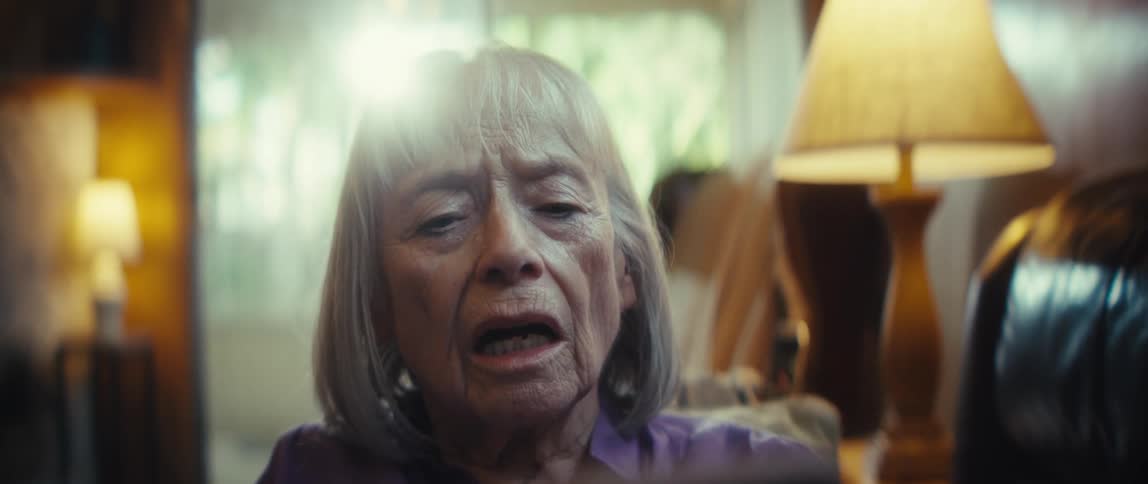 An elderly woman sitting and holding a cellphone looking at it with great sadness