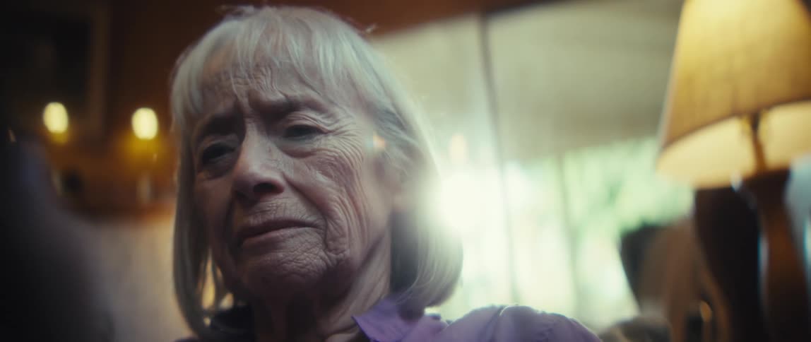 Close up of an elderly woman sadly watching media content on a mobile phone while sitting in a living room during daytime