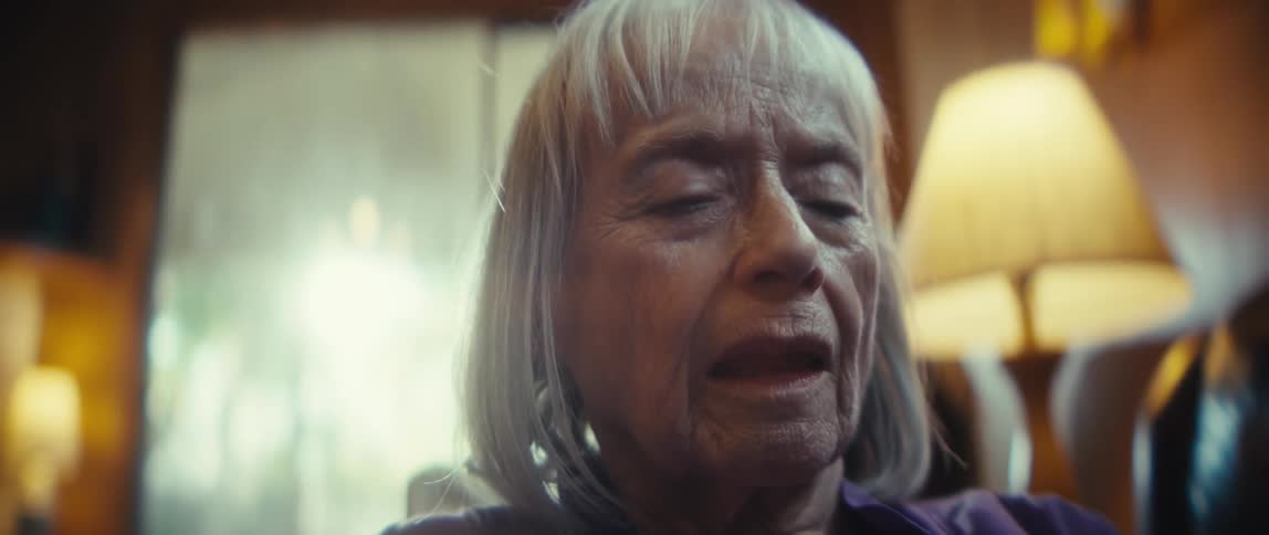 An elderly woman sitting and holding a cellphone looking at it sadly