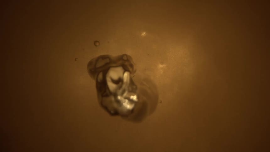 He video features a small bloblike metallic sphere that emerges from the center of a brown background briefly swirling with distorted reflectionsthe object quickly contracts and seems to melt back into the background resembling a droplet of liquid