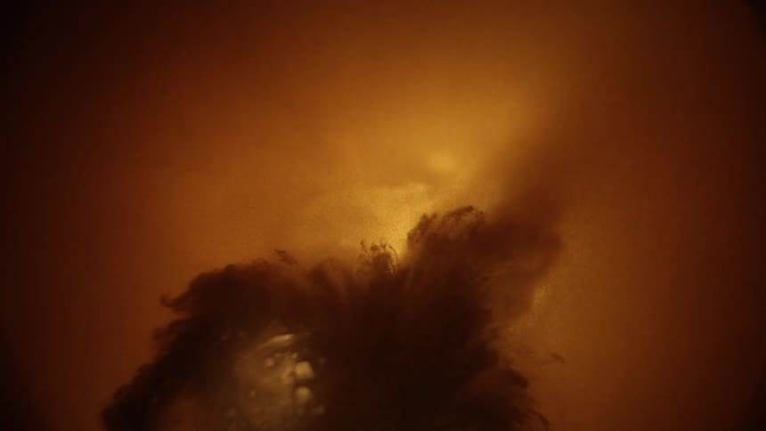 The video is a highly stylized macrolevel shot with a dominant goldenbrown color cast it begins with a closeup of a small shiny metalliclooking object that quickly explodes or dissolves into a cloud of dark shadowy particles against the warm haz