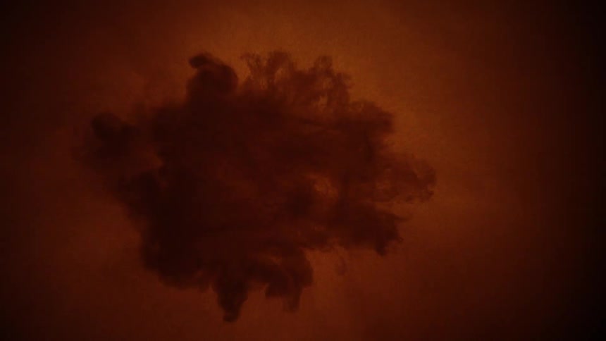 A glowing golden droplet blooms into a circular splash with a dark frilled edge in amber liquid