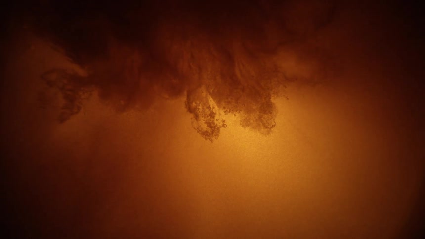 A cloud of dark ink billows downward and disperses into a glowing orange liquid slowly spreading out until it completely fills the frame