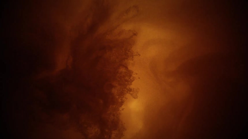 This is a highly magnified stylized macro shot with a dark amberorange background a mass of dark cloudy material emerges from the top and rapidly disperses into particles creating a chaotic smoky effect against the warm lighting