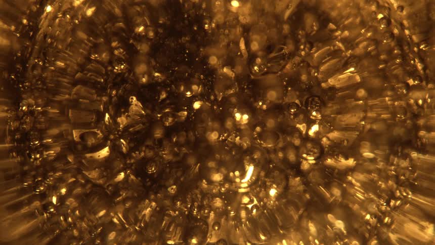 A tight closeup shows the golden bubbles rising and collapsing rapidly in a clear liquid likely a carbonated drink the lighting is warm and bright giving the bubbly liquid an effervescent radiant texture