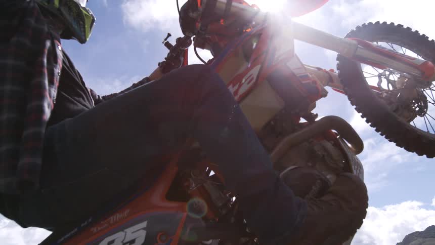 Motorcyclist wearing a helmet lifts an orange bike under the sun
