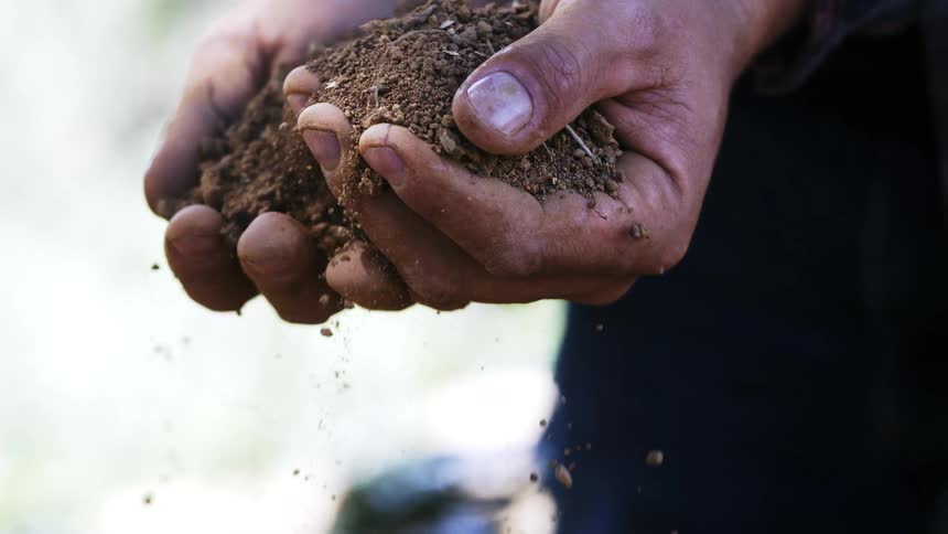 Hands hold loose soil with small rocks as particles fall between fingers