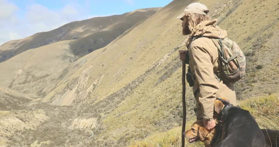 A young male standing outdoors with his dogs while hiking during daytime