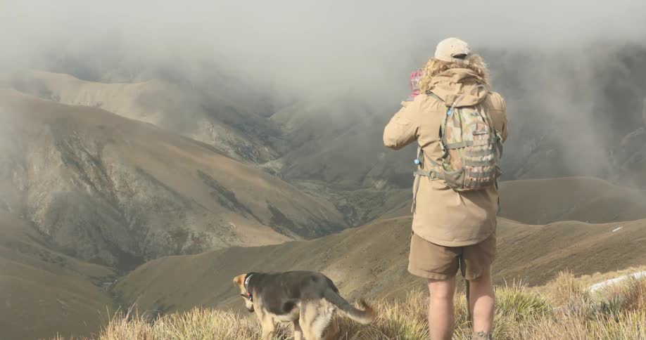 The woman is standing with her dog before the mountains