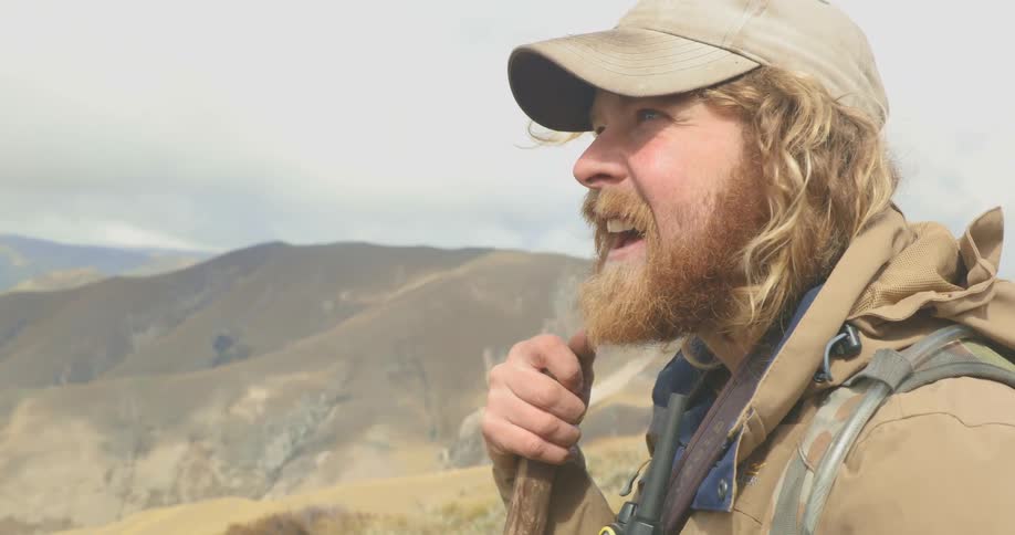 A man with a walking stick and backpack is on top of a mountain looking around