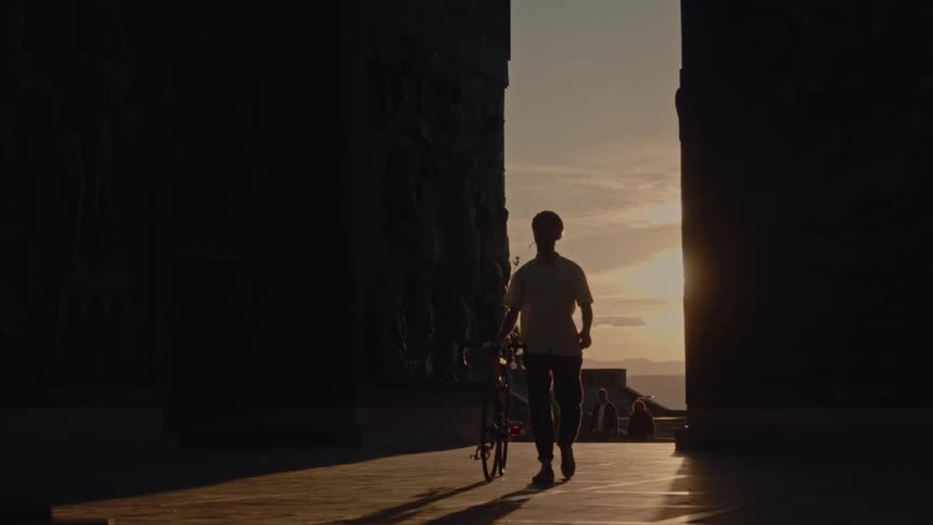 Sunset silhouettes a man walking a bike