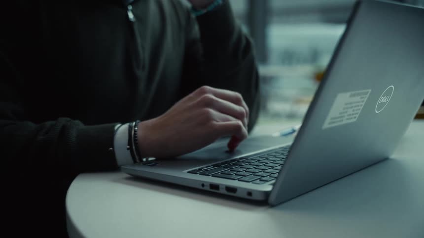 Person types on laptop keyboard at white table beside gray cup with green lid