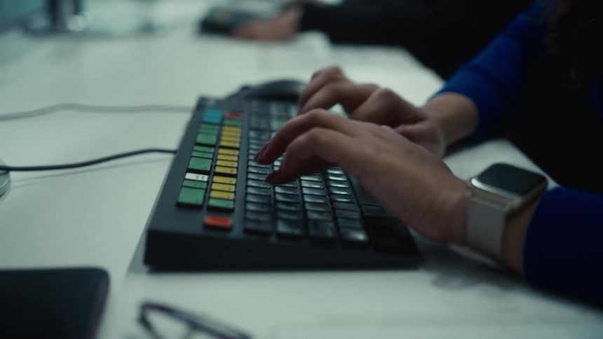 The video is a closeup shot focusing on a persons hands quickly typing on a specialized keyboard that features several colored keys likely a trading or financial terminal keyboardthe person is wearing a blue top and a smartwatch on their wrist sug