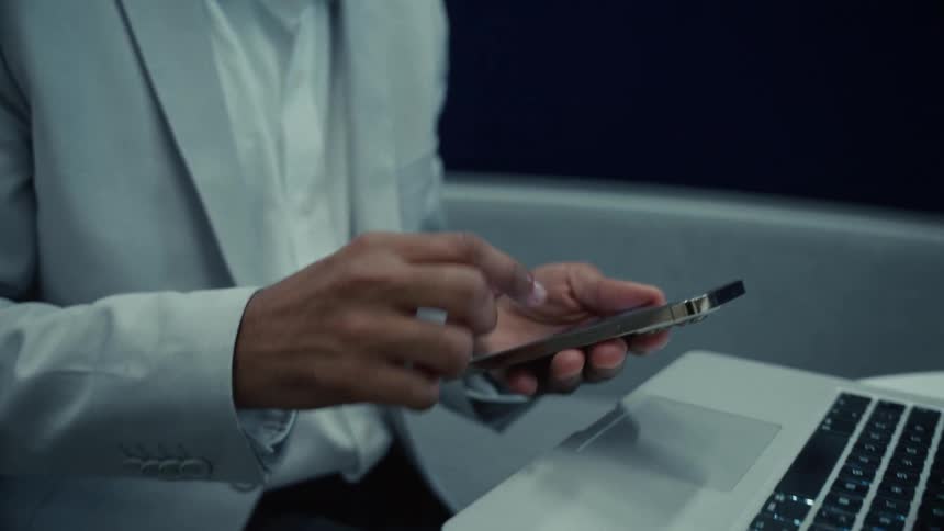 A black adult types on a laptop then scrolls on a smartphone