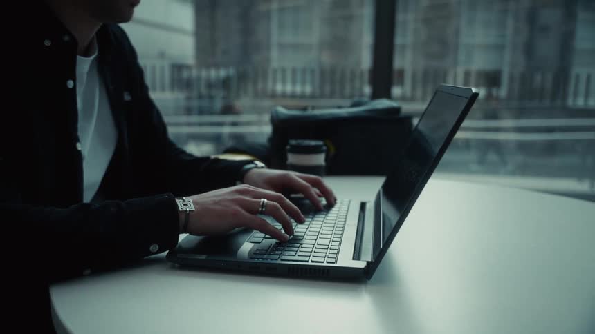 A man sitting at a table opening a laptop and typing on the keyboard