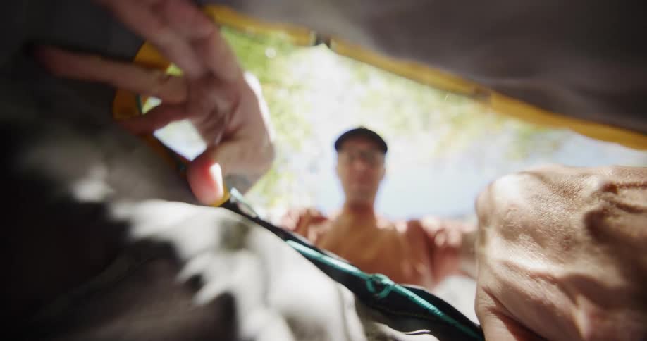 A view from inside a dark backpack shows a pair of hands opening the yellow drawstring closure to reveal a blurred man standing in bright sunlight outside reaching inside the bag