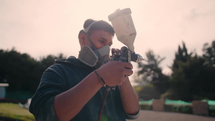Man wears a protective mask while applying paint with a spray gun