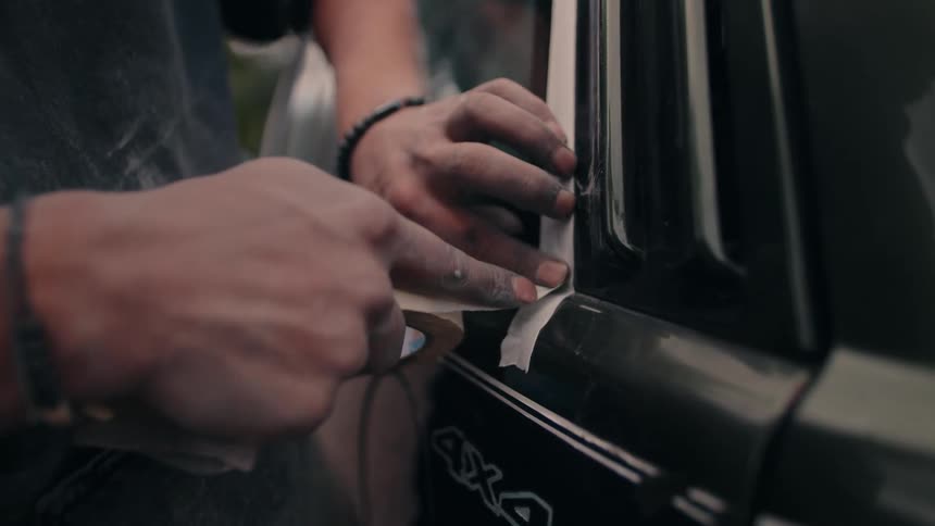 Man applies masking tape along edge of dark suv window with visible 4x4 decal