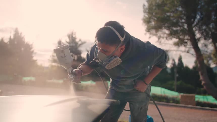 Man painting a car with a paint sprayer wears a respirator mask