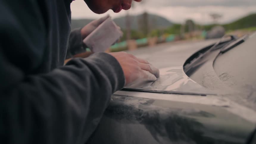 The man blows the dust after sanding the car