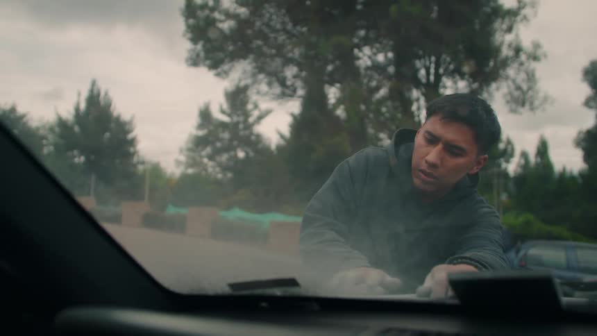 The man is sanding the car outside