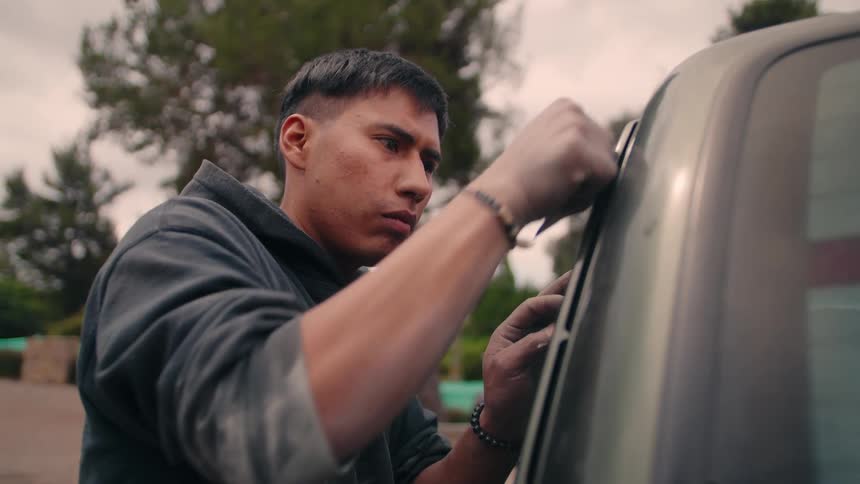 Man concentrates while working on sanding a vehicle on an overcast day