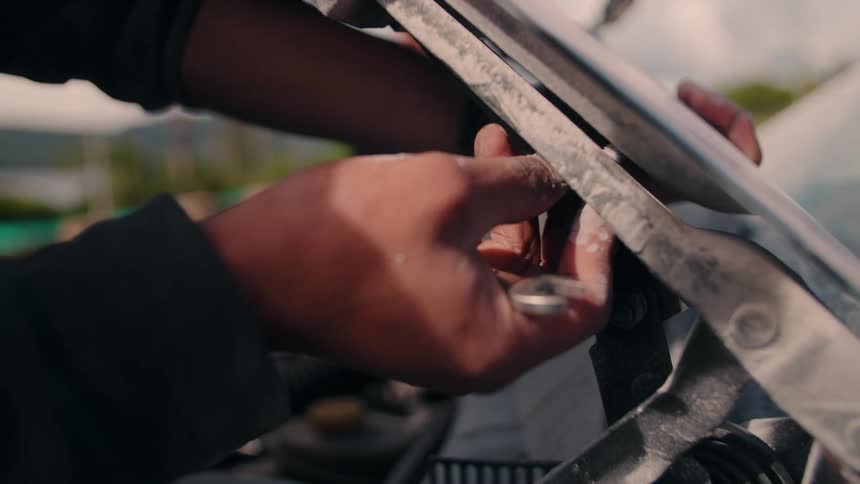 Man adjusts mechanical component with wrench in vehicle engine compartment outdoors