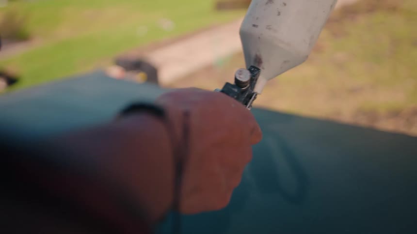 Hand holds a paint spray gun applying white paint on a metallic surface