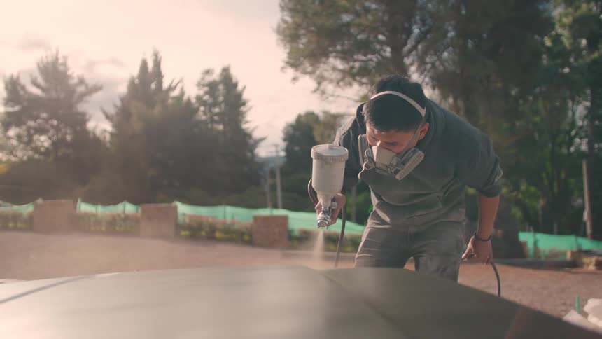 The man is using a paint gun to spray the car