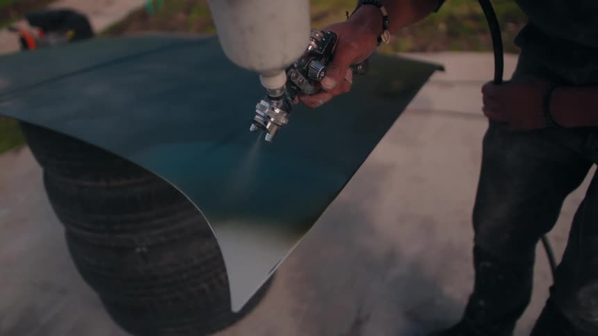 A man is using a paint sprayer to spray paint on a large piece of metal