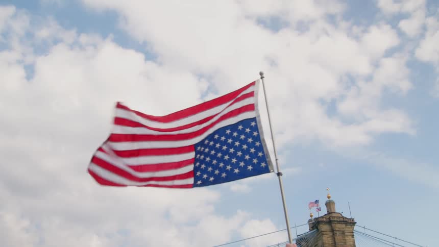 Upside down united states flag waves in the wind against partly cloudy sky with bridge in background