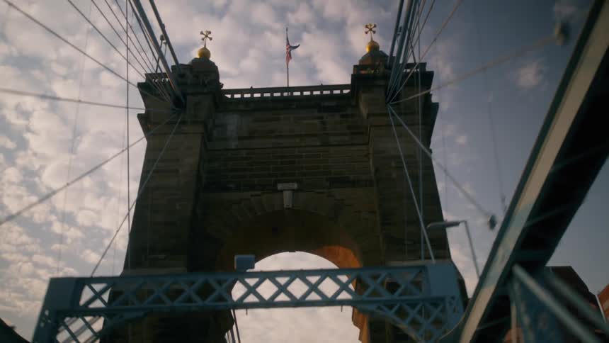 Stone bridge with golden domes and american flag stands out in suspension bridge structure over the river