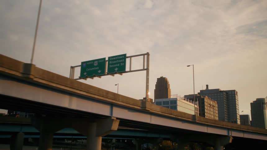 A city highway overpass and skyline pass by against a warm hazy sunset