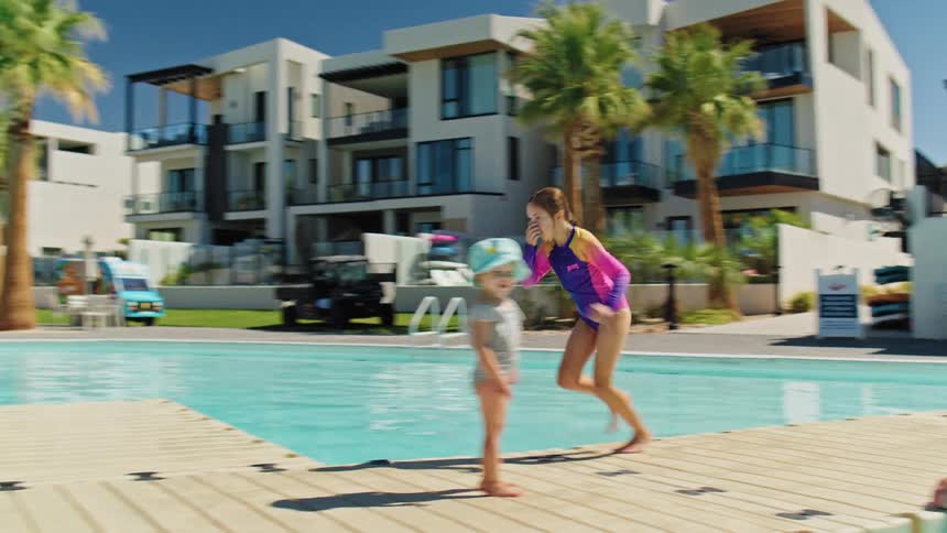 Young girl jumps off the deck into the pool on a sunny day surrounded by palm trees