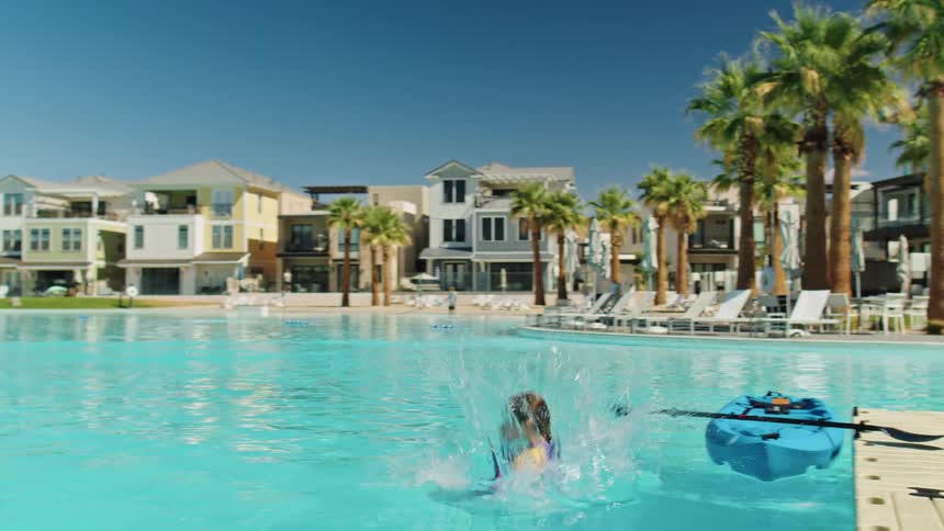 Young girl running off deck and jumping into pool at a resort