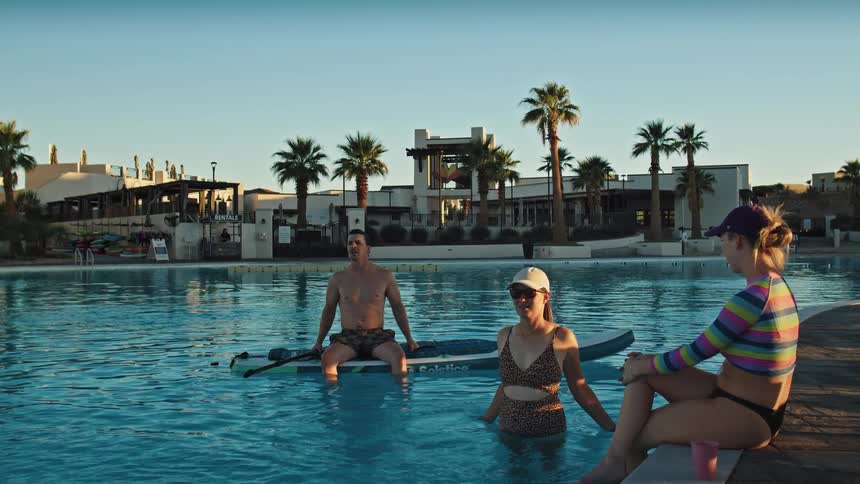 Three friendstwo women and a manrelax in a public pool at midday during their vacation engaged in a lively discussion as they enjoy the water together