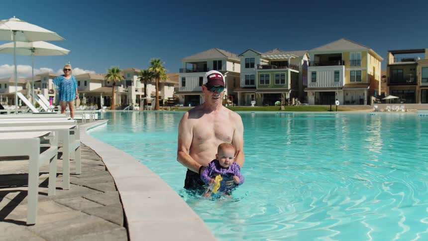 The father is dipping his happy baby in the pool