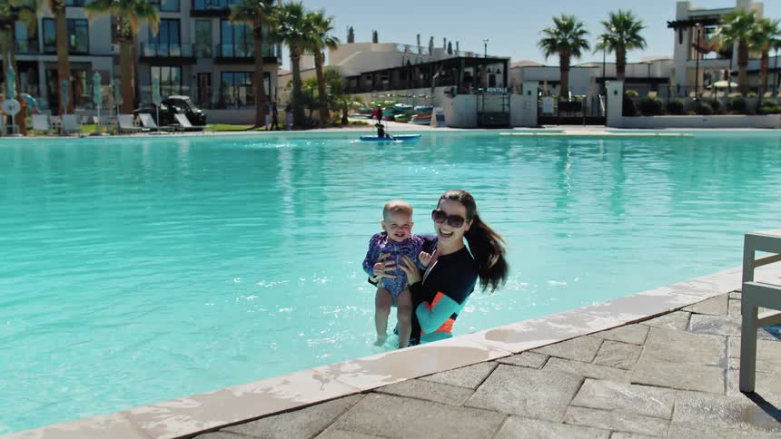 Woman smiles while lifting her young daughter in the pool under the sun