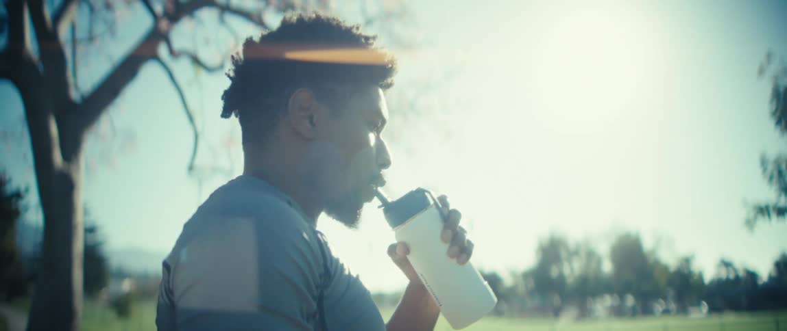 Man straightens from a picnic table in the park and drinks from a reusable beverage container on a sunny day in autumn