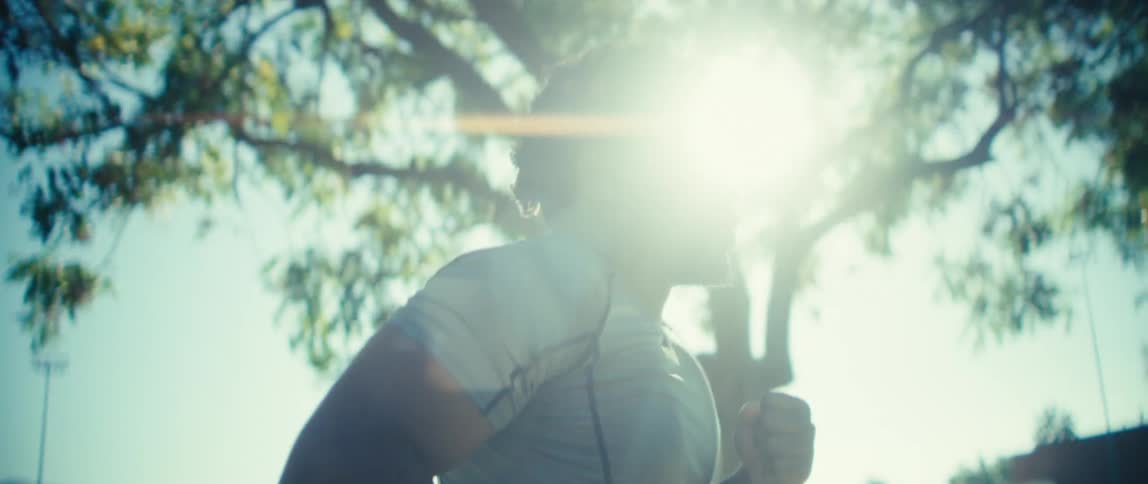 Man runs outdoors under blue sky and bright sun with trees in the background and a sense of motion and energy