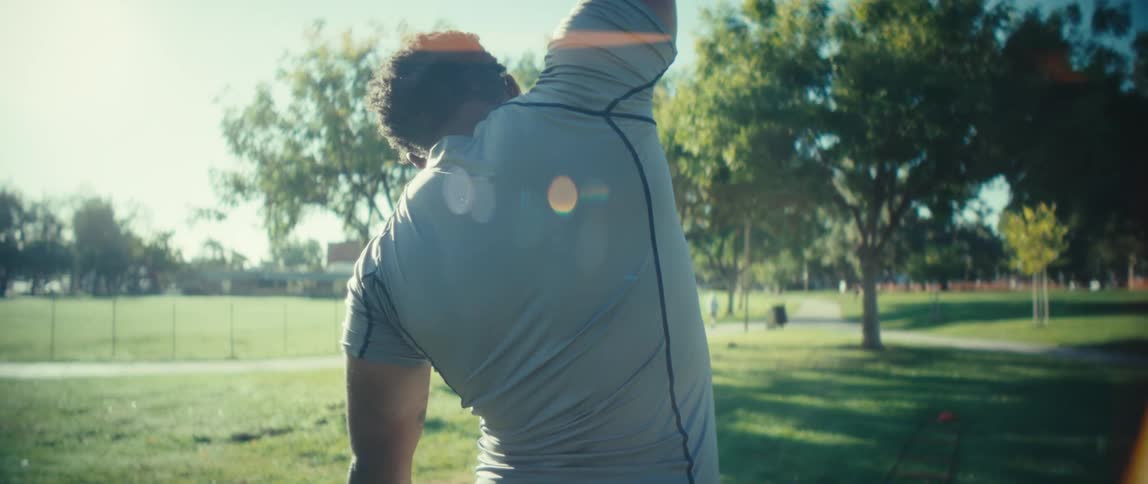 A man is standing in the grass at a park stretching his arms