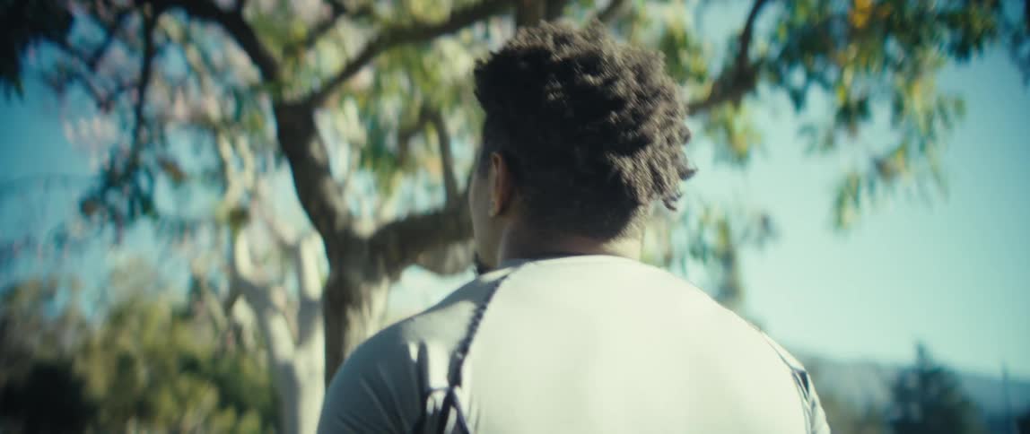 Man holds a football under the trees on a sunny day