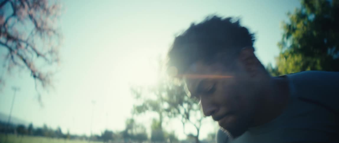 Man leans forward with focused expression in outdoor setting lit by sunlight through trees