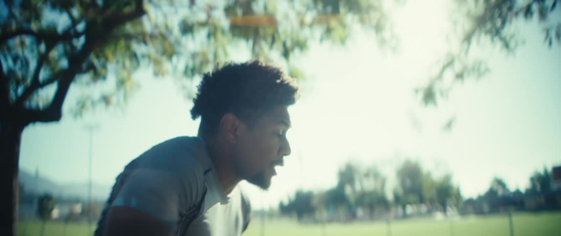 A man carring a football is running practice drills in a park