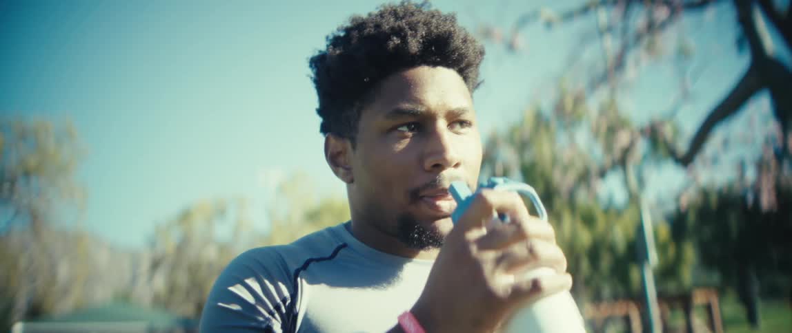 Man breathes deeply and takes a sip from a container while standing in the park on a sunny day in autumn