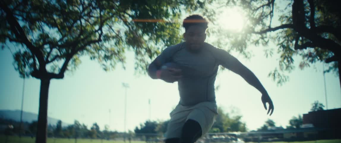 Silhouetted against the bright sun an athlete practices football drills running back and forth under a large tree